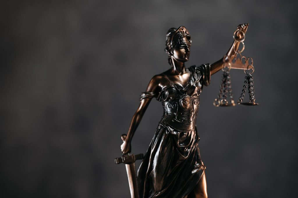 themis-sculpture-with-libra-8112201 Detailed bronze Lady Justice statue with scales and sword against a dark background, symbolizing law and justice.